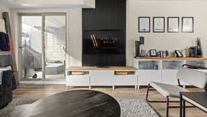A modern living room with a large flat-screen TV, a sliding glass door leading to a balcony, and a minimalist design with a white console and grey furniture. - 9 Peaks | Scandinavian | Pool | Hot Tub | Beach (Invermere)