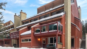 A multi-story building with balconies, a covered porch, and a snow-covered ground. - Nature`s Nook | Ski In/Out | Pools | Hot Tub (Panorama)