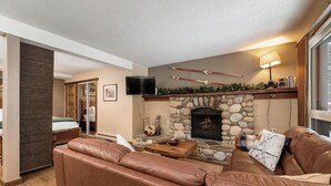 A living room with a stone fireplace, leather sofa, and a television on the wall. - Nature`s Nook | Ski In/Out | Pools | Hot Tub (Panorama)