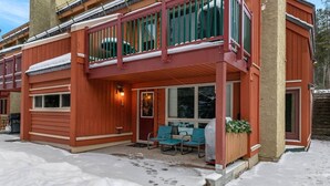 A two-story wooden building with a balcony, outdoor seating, and a snow-covered ground. - Nature`s Nook | Ski In/Out | Pools | Hot Tub (Panorama)