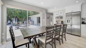 Una cocina moderna con un refrigerador de acero inoxidable, un comedor con mesa y sillas de madera, y un puerta corrediza de vidrio que da a un patio exterior.