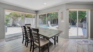 Un comedor con mesa y sillas, ventanas amplias y vista a un jardín trasero con piscina.