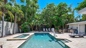 Una piscina rectangular con agua cristalina, rodeada por una zona de patio con sillones de descanso y una mesa de comedor.