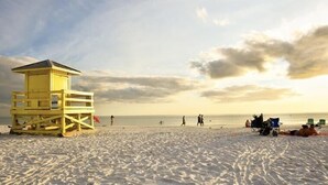 Una playa con una torre de salvavidas, arena y algunas personas.