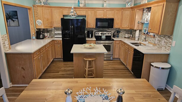 A kitchen with wooden cabinets, a black refrigerator, a stove, and a microwave. - Beautiful Warm Beach House Retreat, King bed, fireplace and Pool (Shreveport)