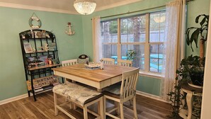 A dining area with a wooden table and chairs, a chandelier, and a window with curtains. - Beautiful Warm Beach House Retreat, King bed, fireplace and Pool (Shreveport)