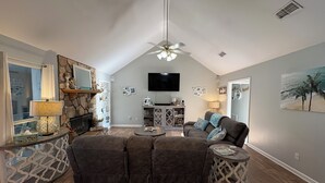 A spacious living room with a high ceiling, a fireplace, a television, and a beach-themed wall art. - Beautiful Warm Beach House Retreat, King bed, fireplace and Pool (Shreveport)