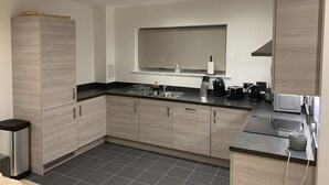 Une cuisine moderne avec des meubles de couleur bois clair, un plan de travail noir, une cuisinière encastrée et une fenêtre au-dessus de l’évier.
