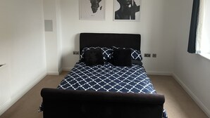 Une chambre à coucher avec un lit, deux œuvres d’art accrochées au mur et une fenêtre avec des rideaux.