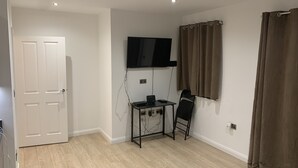 Une pièce avec une porte blanche, un téléviseur fixé au mur, un bureau avec une chaise et une fenêtre avec des rideaux marron.