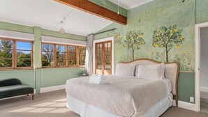 A bedroom with a large bed, a bench, and a view of trees through the window.