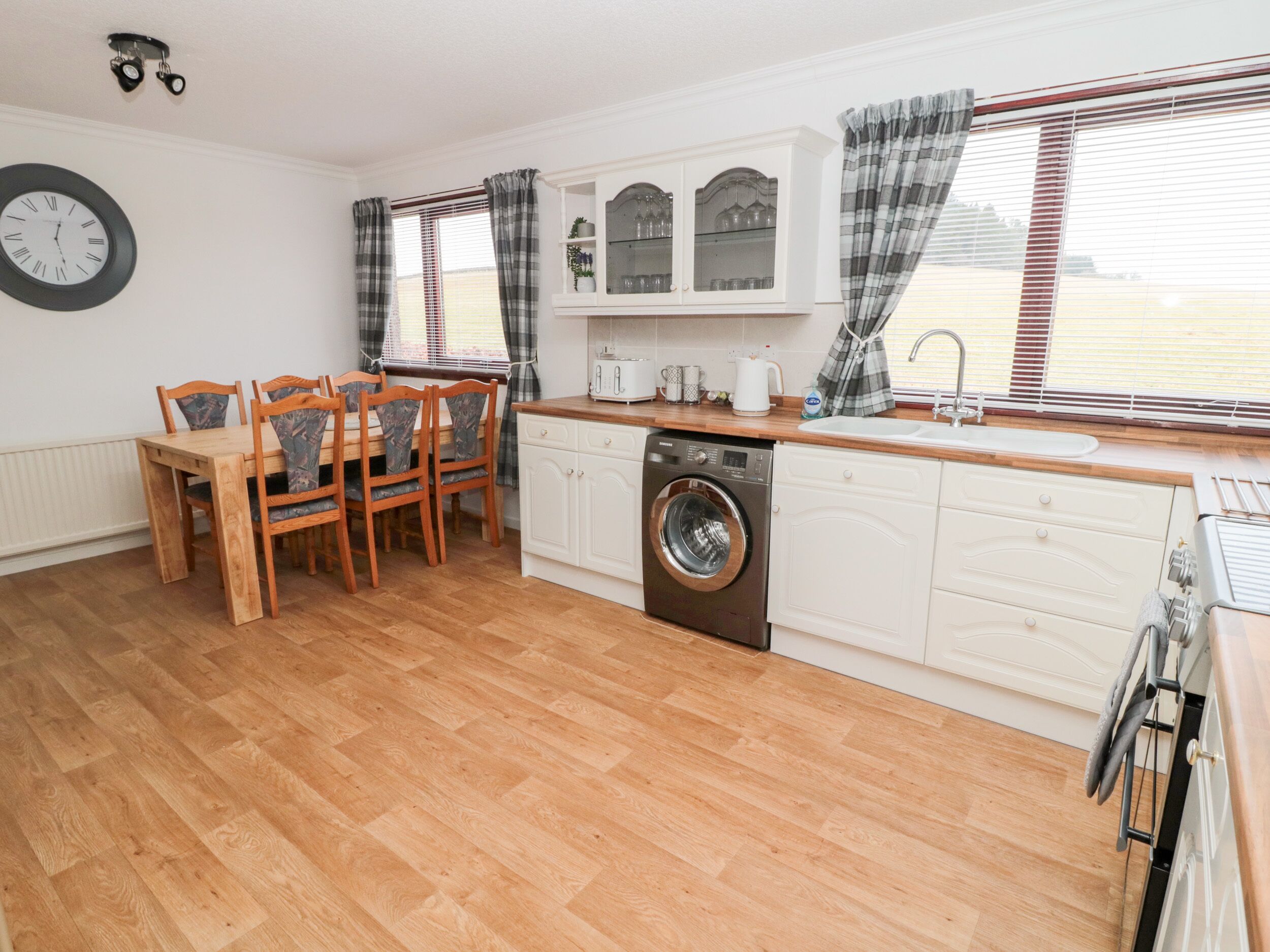 Une cuisine compacte avec une table et des chaises en bois, un lave-linge encastré et une fenêtre avec des stores.