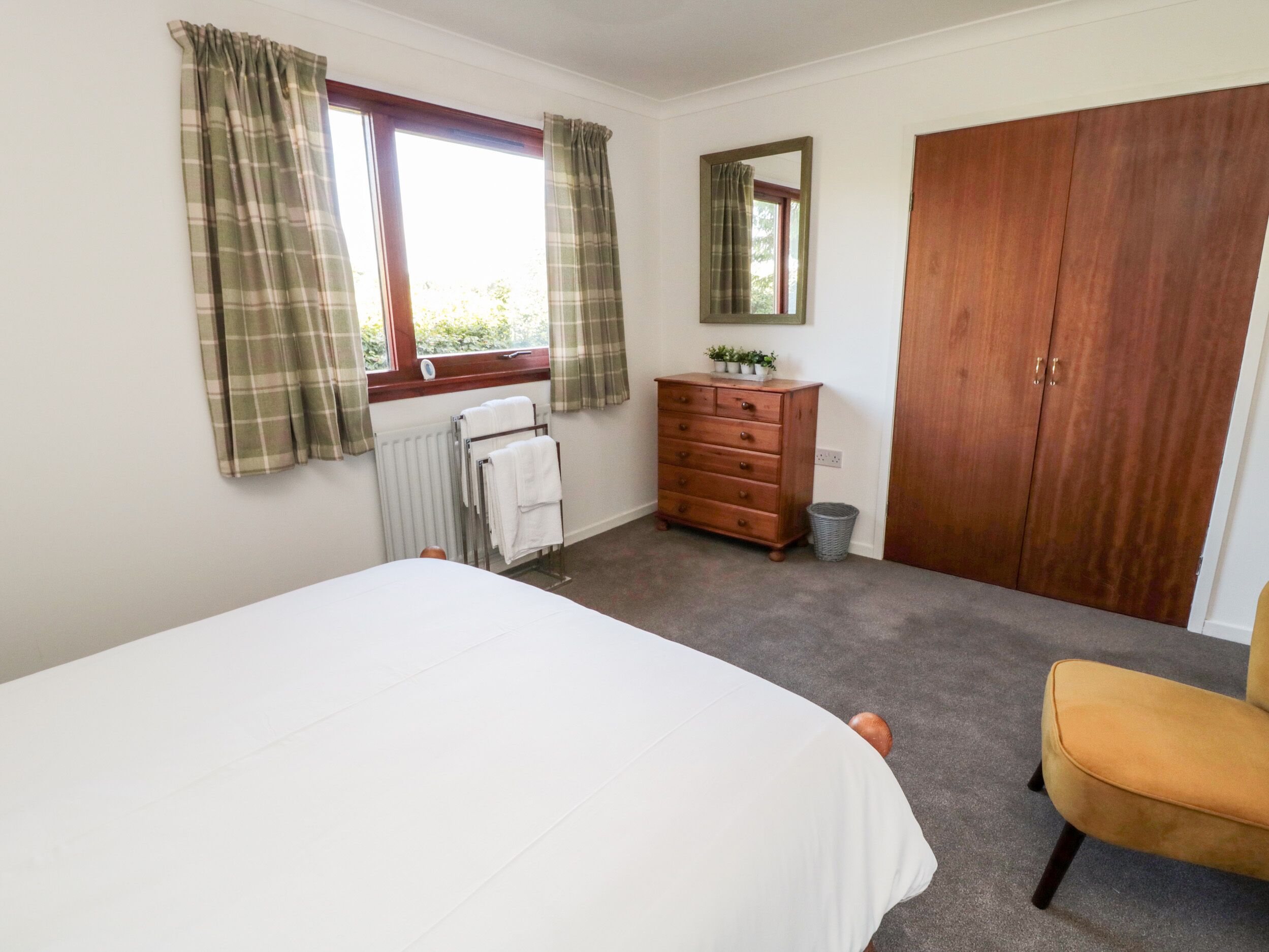 Une chambre à coucher comprenant un lit, une commode en bois, une armoire en bois, un radiateur et une fenêtre avec des rideaux.
