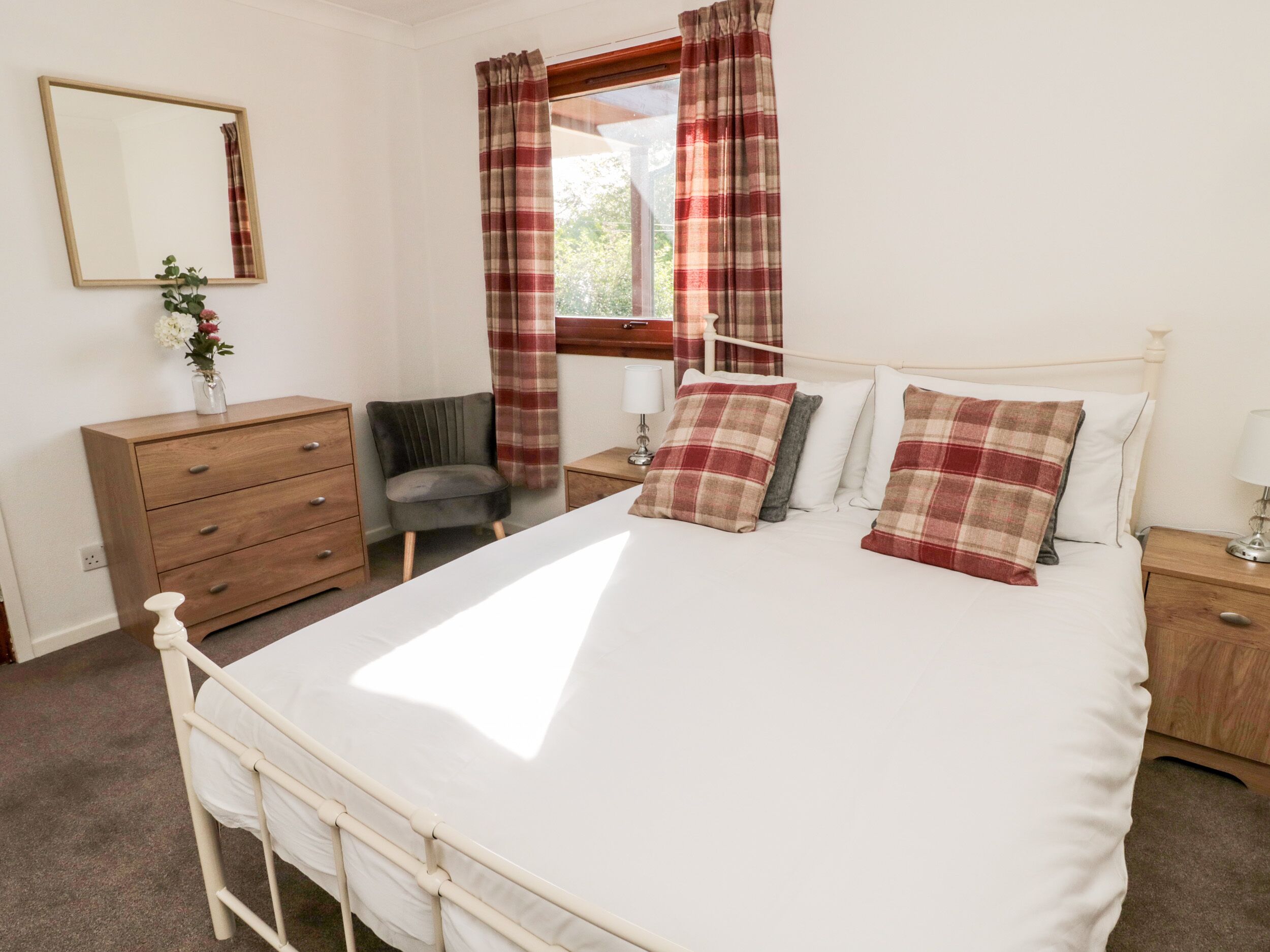A bedroom with a bed, a dresser, a chair, a nightstand, a lamp, a mirror, and a window with curtains.