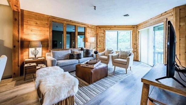 A cozy living room with wooden walls, a sofa set, a coffee table, and a television. - Ski in/Ski out Modern Chic Condominium (CHAMPION)