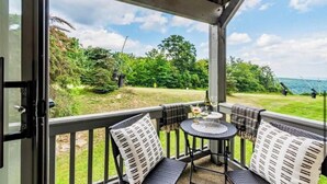 A covered outdoor seating area with a table and chairs, overlooking a grassy landscape and a body of water. - Ski in/Ski out Modern Chic Condominium (CHAMPION)