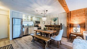 A modern kitchen with stainless steel appliances, a wooden dining table with chairs, and a chandelier. - Ski in/Ski out Modern Chic Condominium (CHAMPION)