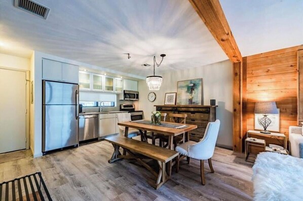A modern kitchen with stainless steel appliances, a wooden dining table with chairs, and a chandelier. - Ski in/Ski out Modern Chic Condominium (CHAMPION)