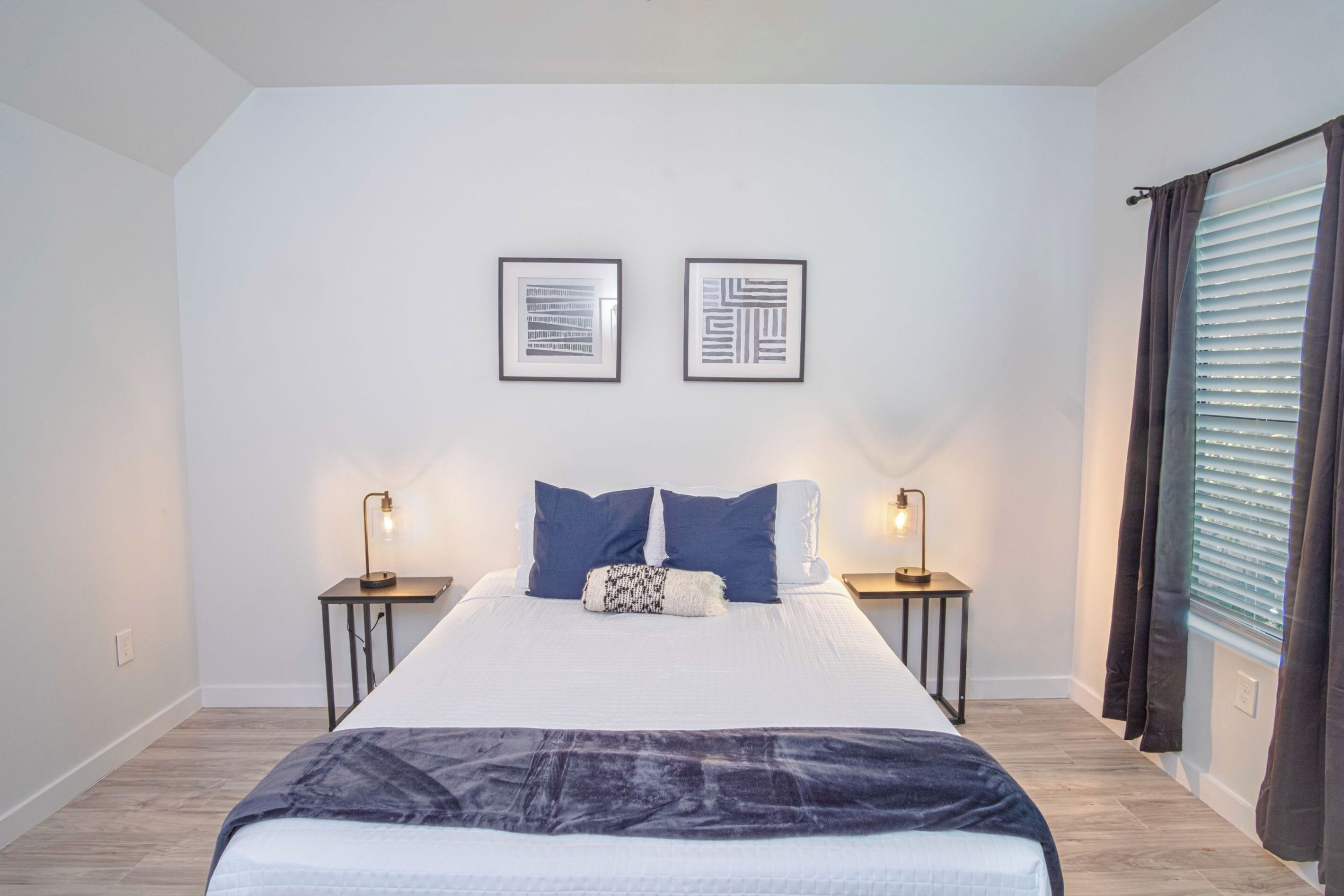 Un dormitorio moderno con una cama grande, dos mesitas de noche y dos cuadros enmarcados en la pared.