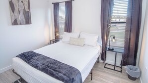 Ein Schlafzimmer mit einem Bett, zwei Nachttischen, einer Lampe, einem Fenster mit Vorhängen und einem Wandbild.
