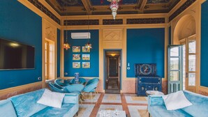 Ein Zimmer mit blauen Wänden, einem Flachbildfernseher, einer Kristallleuchter und einem blauen Sofa.