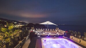 Eine Dachterrasse mit Whirlpool, Sitzgelegenheiten im Freien und Blick auf das Meer bei Nacht.