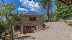 Une maison en pierre avec un toit en tuiles, des volets en bois et une allée gravillonnée.