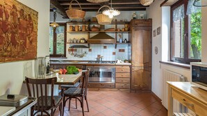 Een keuken met een eettafel, stoelen, een fornuis en een raam met uitzicht op groen.