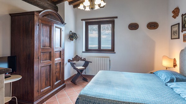 Un dormitorio con cama, un armario de madera, un radiador, una ventana con cortinas de encaje y una pared decorada con platos.