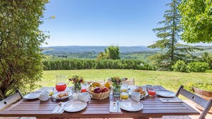 Una tavola di legno apparecchiata per la colazione, con vista panoramica su dolci colline e cielo sereno.