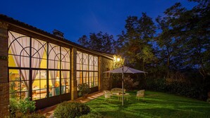 Une maison bien éclairée, dotée de grandes fenêtres, d’une terrasse avec des chaises et d’un jardin.