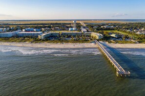 An aerial view of a coastal area with a long pier extending into the water, surrounded by buildings and a beach.