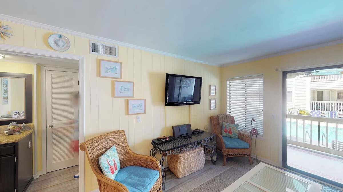 A living room with a television, wicker chairs, a small table, and a view of the outside.
