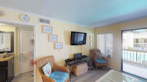 A living room with a television, wicker chairs, a small table, and a view of the outside.