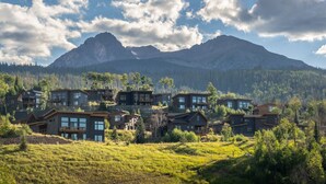 A cluster of modern houses with large windows, set against a backdrop of mountains and a clear sky.