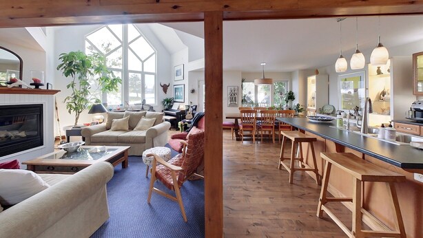 Ein geräumiger Wohnbereich mit Kamin, großem Fenster und einer Küche mit Holzbarhocker und Bar.