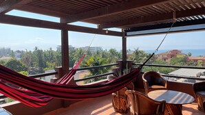 Un balcon avec un hamac, des chaises en bois et une table.