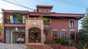 Une maison à deux étages, avec un toit en tuiles, un balcon et une entrée fermée par un portail.