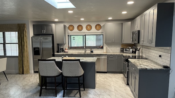A modern kitchen with grey cabinets, a central island with bar stools, a built-in oven, and a skylight. - 5 mi to WEC, 10 to HITS -spacious house sleeps 10, big kitchen & 2 sitting areas (Ocala)
