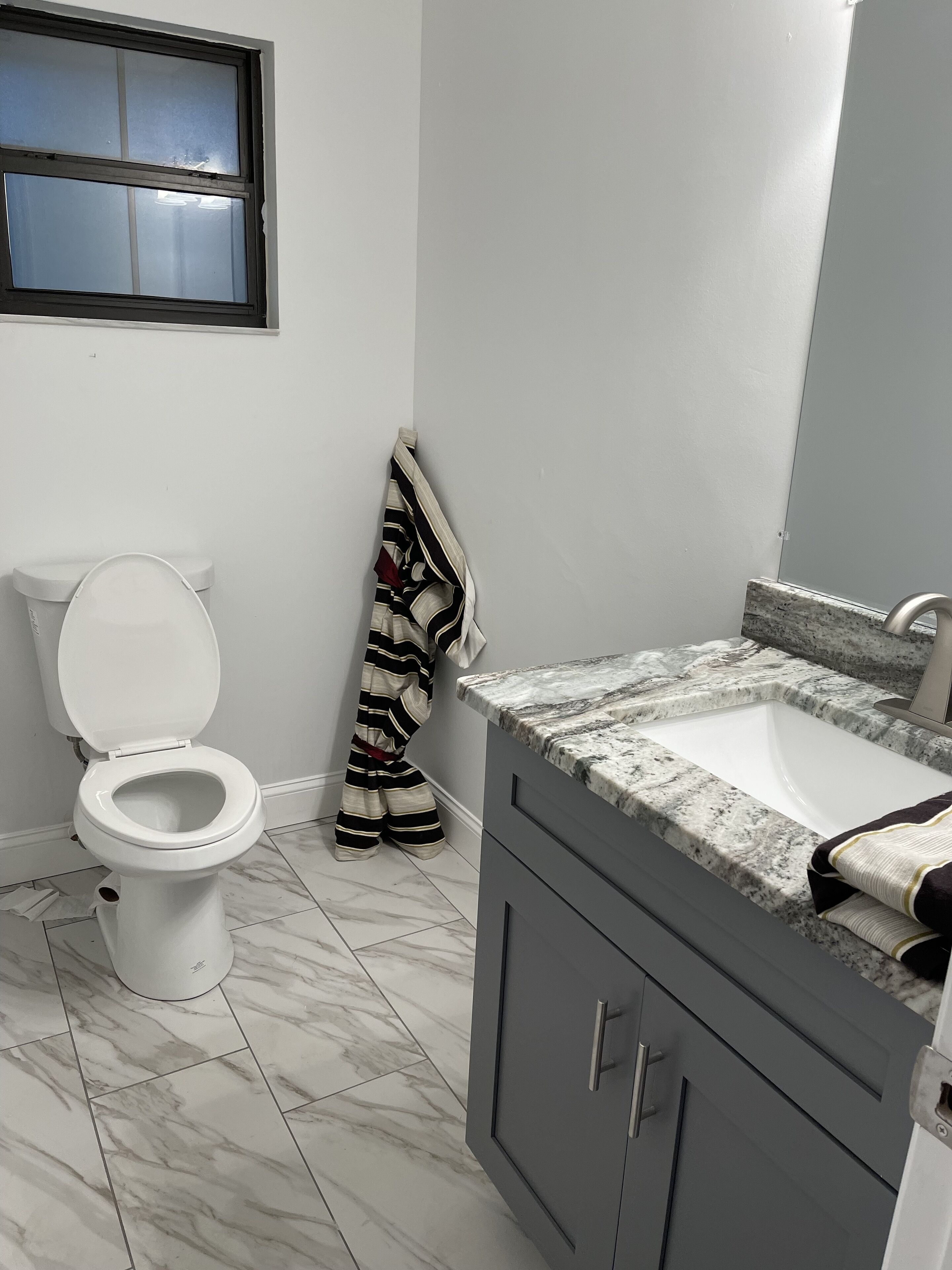 A bathroom with a white toilet, a striped towel hanging on the wall, and a marble sink with a faucet.