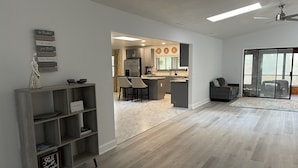 A spacious living area with a kitchen in the background, a sliding glass door leading to a patio, and a bookshelf with motivational signs. - 5 mi to WEC, 10 to HITS -spacious house sleeps 10, big kitchen & 2 sitting areas (Ocala)
