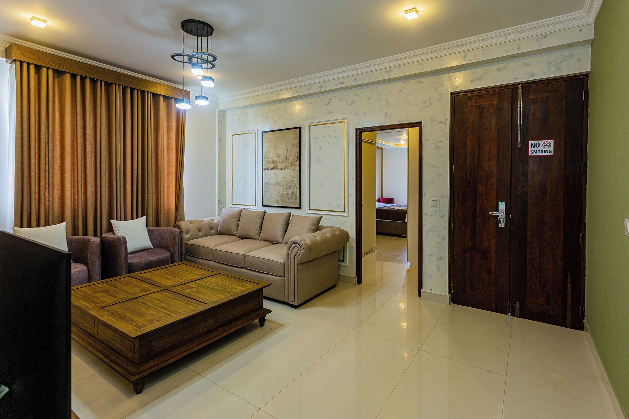 A living room with a sofa set, a coffee table, and a television. There is a door with a 'No Smoking' sign.