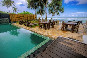 Un área de piscina con terraza de madera, sillas de descanso y vista al océano.