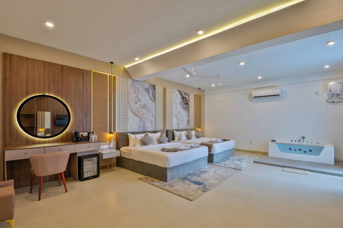 A modern bedroom with a large bed, bedside tables, a desk, a chair, a vanity, and a bathtub.