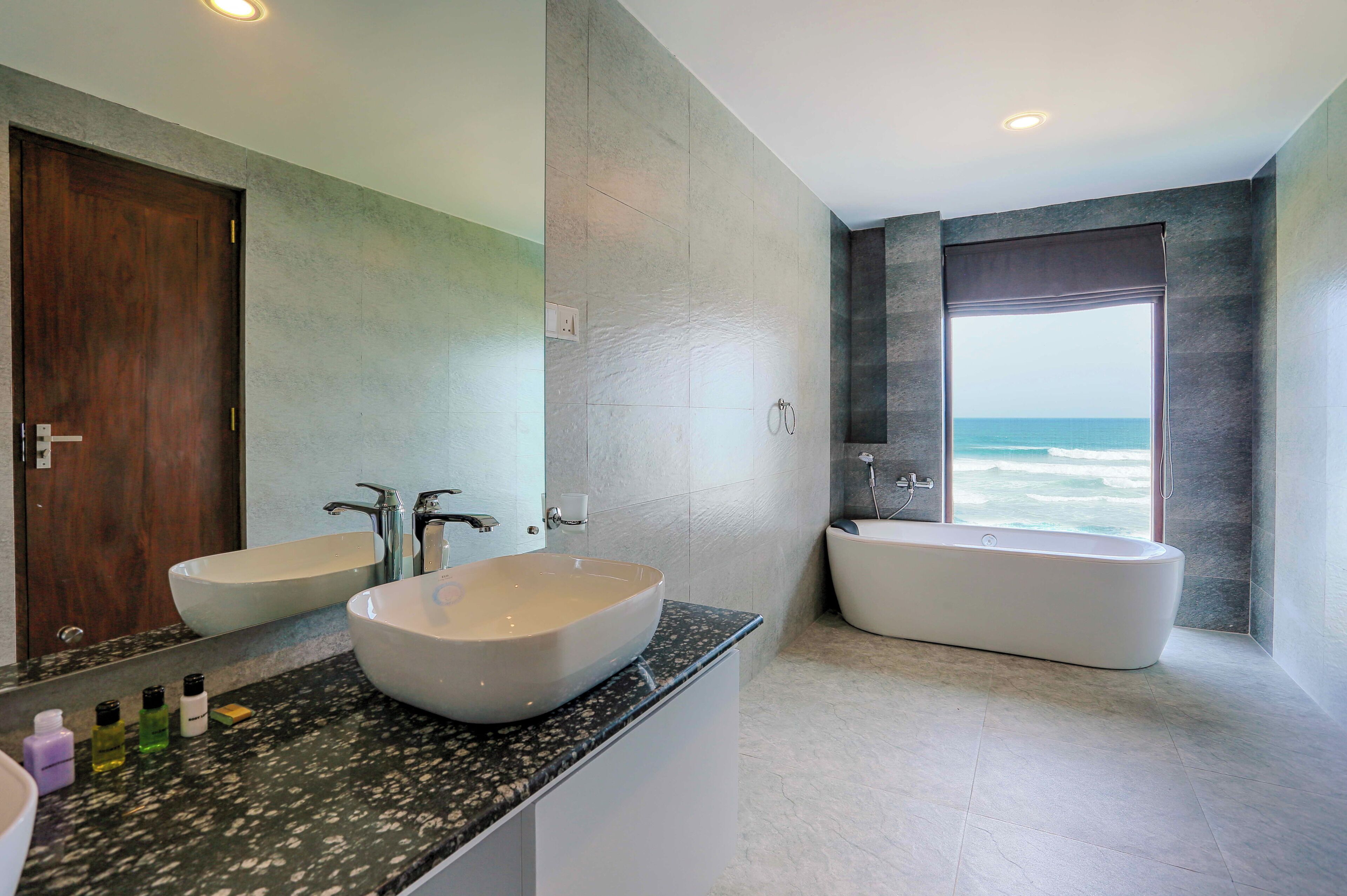A modern bathroom with a large mirror, two sinks, a bathtub, and a view of the ocean.