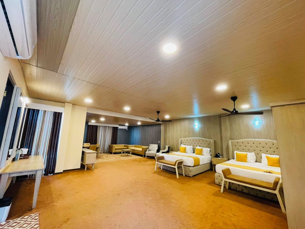 A hotel room with a large bed, two smaller beds, a sofa, a desk, and a chair.