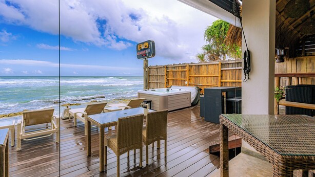 Una terraza de madera con mobiliario de mimbre, un jacuzzi y un cartel que indica un restaurante.