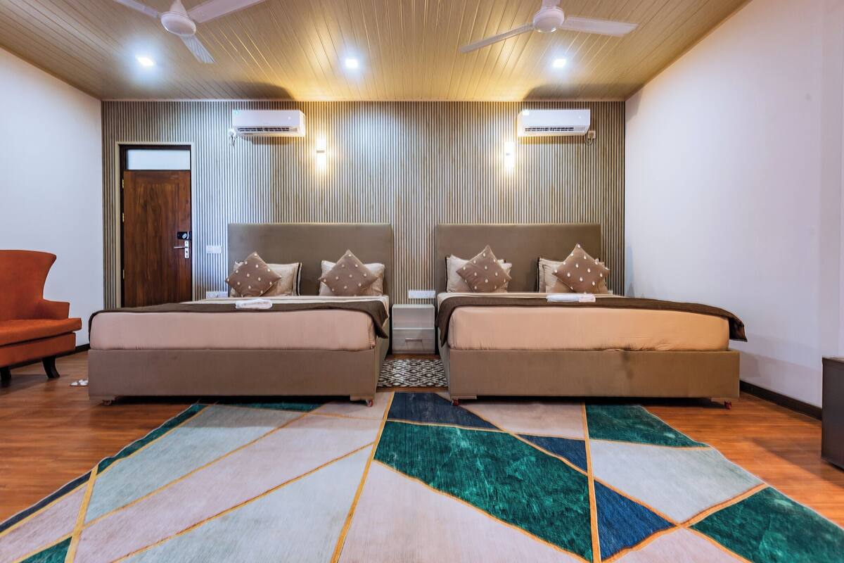 A hotel room with two beds, a sofa, a patterned rug, and ceiling fans.