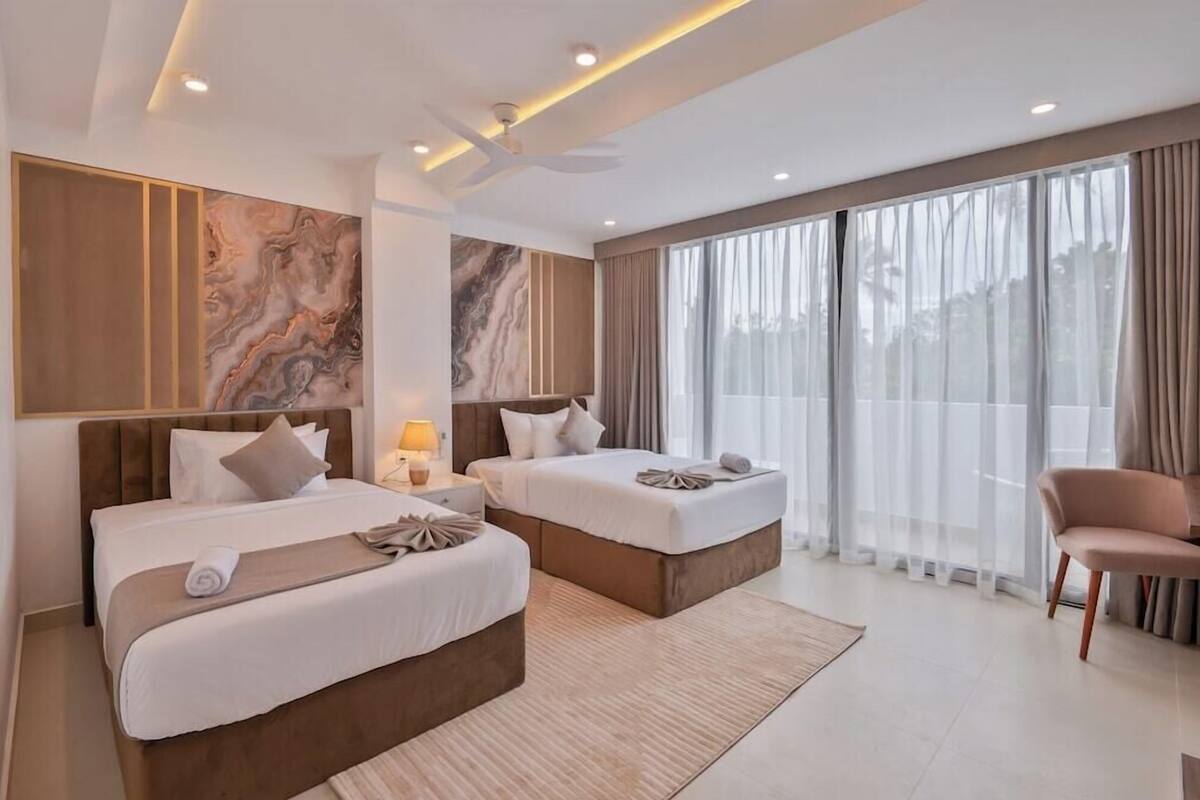 A modern hotel room with two beds, a large window with curtains, a ceiling fan, and a nightstand with a lamp.
