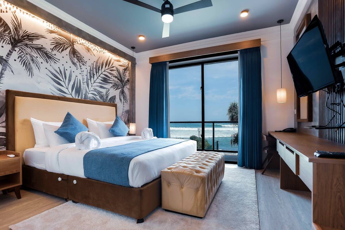 A modern hotel room with a large bed, a desk, and a view of the ocean.